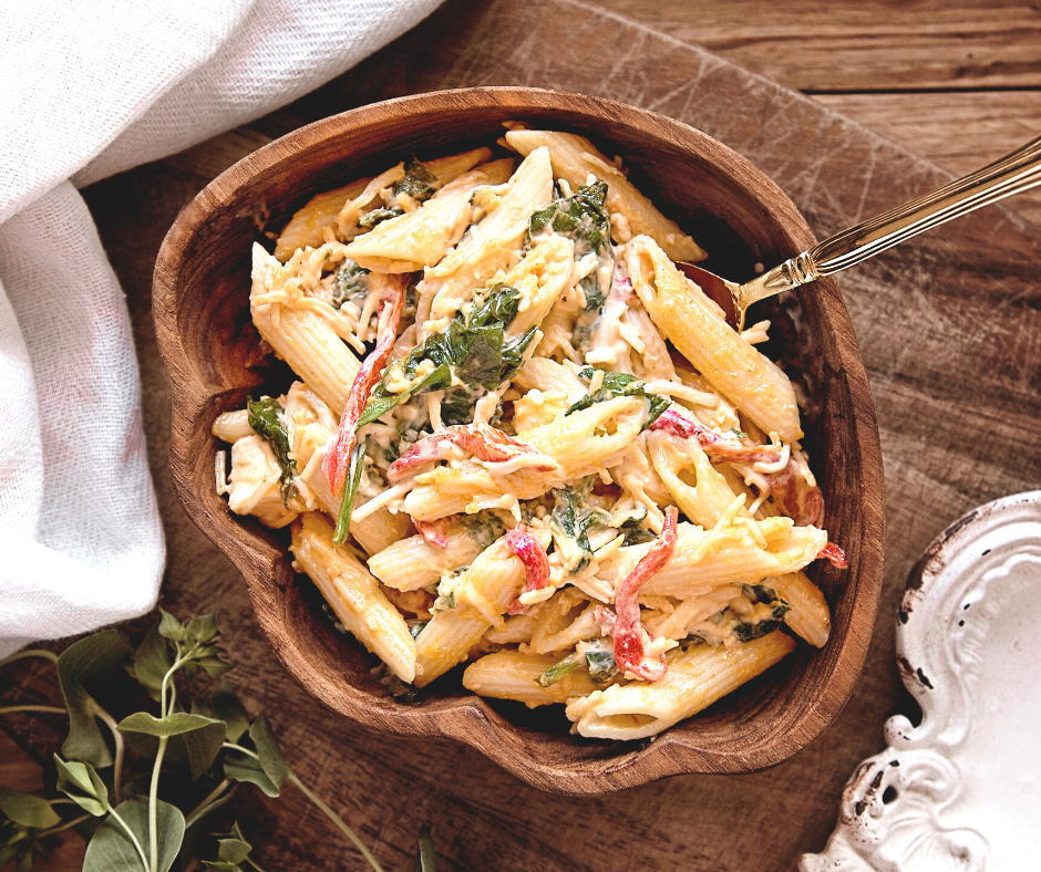 a wooden bowl full of cooked pasta with sauce and veggies and a utensil ready to eat.